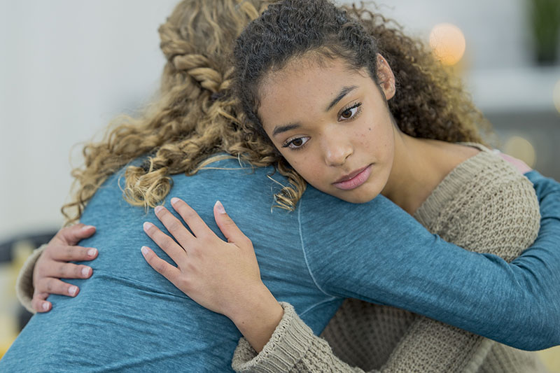 A young woman embraces another person while she stares blankly